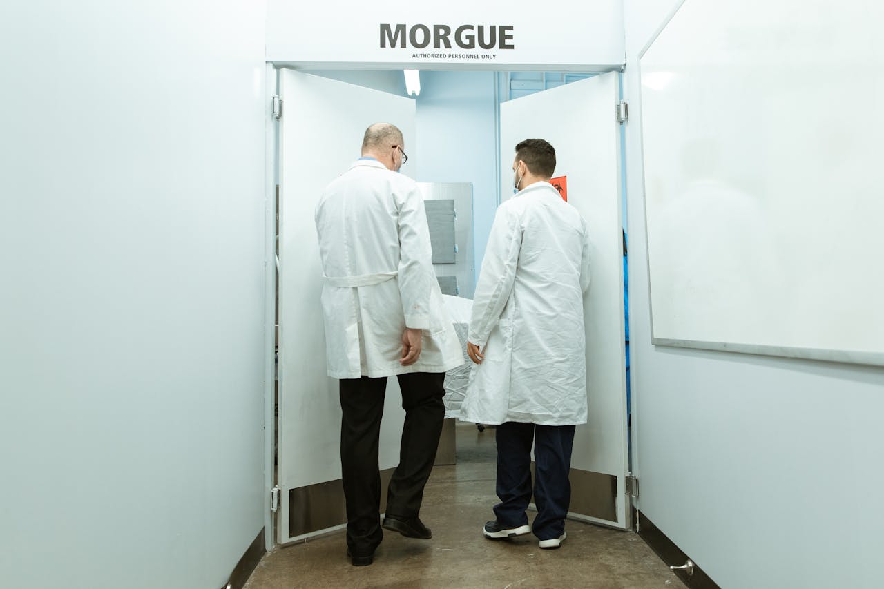 Medical professionals in lab coats entering a morgue with a body on stretcher.